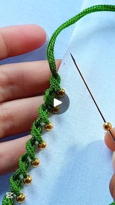 someone is working on something with green thread and gold balls in the middle of it