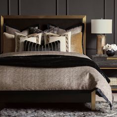 a bed with black and gold pillows on top of it next to a night stand