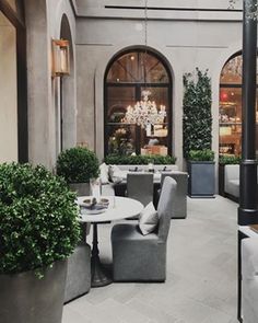 an outdoor seating area with potted plants and chandeliers in the background,