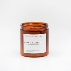 a candle with a label on it sitting in front of a white background that says moss and amber