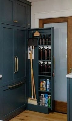 an open cabinet in the middle of a kitchen with brooms and cleaning supplies inside