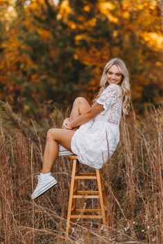 a woman sitting on top of a wooden ladder in the middle of some tall grass