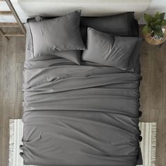 a bed with grey sheets and pillows in a room