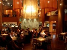 people sitting at tables in a restaurant with lights hanging from the ceiling and windows above them