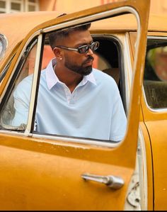 a man sitting in the driver's seat of a yellow car looking out the window