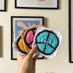 a hand holding two crocheted coasters in front of pictures on the wall