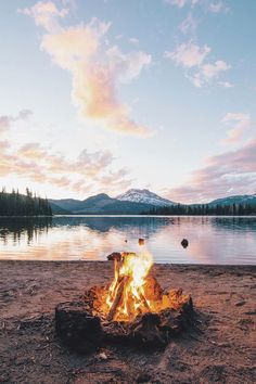 a campfire on the shore of a lake at sunset