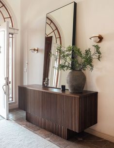 a large mirror sitting on top of a wooden cabinet next to a vase filled with flowers