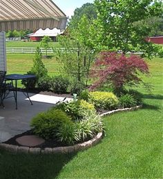 an outdoor patio with table and chairs in the grass next to trees, bushes and flowers