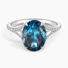 a blue diamond ring with diamonds on the sides and an oval cut stone in the middle