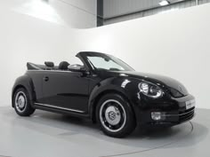 a black convertible car is parked in a white room with no one around it and the roof down