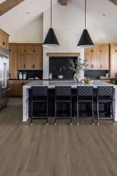 a large kitchen with wooden floors and black chairs in front of an island counter top