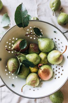 a white colander filled with green pears and leaves