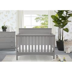 a baby crib in a room with white walls and grey furniture, including a potted plant