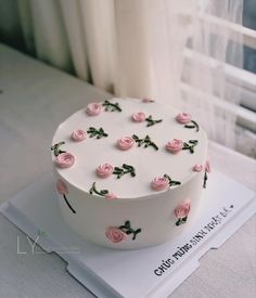 a white cake with pink roses on it sitting on top of a table next to a window