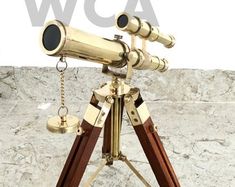 an antique brass telescope with wooden tripod stands in front of a stone wall