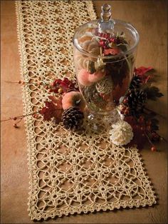 a glass vase filled with flowers on top of a lace doily next to pine cones and berries