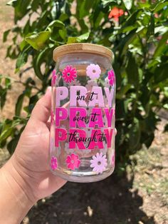 a hand holding up a jar with pink and white flowers on it that says pray