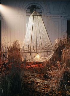 a light hanging from the ceiling in a room filled with plants and dead grass on the ground