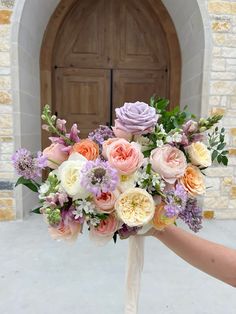 a bridal bouquet is held in front of a church door with the bride's hand holding it