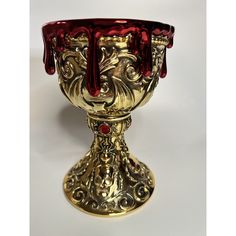 an ornate gold and red glass cup on a white surface with blood dripping from the top