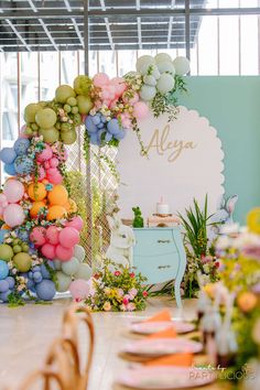 a room filled with lots of colorful balloons and flowers on the wall next to a table