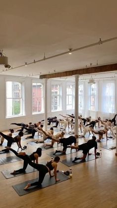 a large group of people doing yoga in a room with wooden floors and white walls