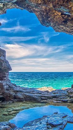 the view from inside an ocean cave looking out at the blue water and rocky shore