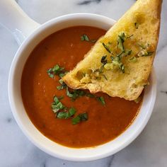 a white bowl filled with soup and a piece of bread sticking out of the side