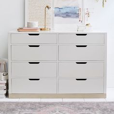 a white dresser with drawers and pictures on the wall