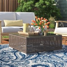 an outdoor living area with couches, table and flowers in vases on rug