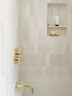 a bathroom with white tile and gold fixtures, including a tub shower faucet