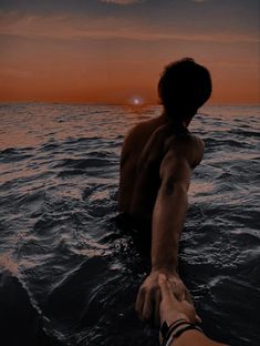 a man standing in the ocean at sunset with his arm out to the side,