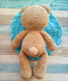 a crocheted teddy bear sitting on top of a wooden floor next to a blue blanket