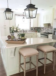 a kitchen island with stools in front of it and two lights hanging over the top