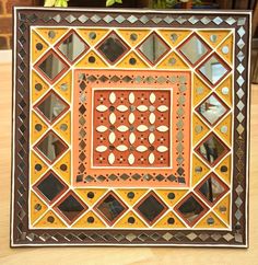 an orange and black decorative tile on a wooden table next to a potted plant