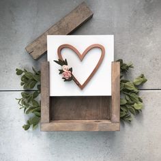 a wooden frame with a heart and flower on it next to some greenery in the shape of a box