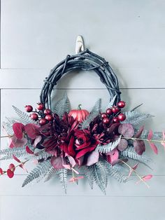 a wreath with red flowers and greenery hanging on a wall