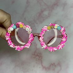 a hand holding up a pair of pink sunglasses with letters on the side and round frames