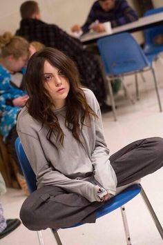 a woman sitting on top of a blue chair in a room filled with other people