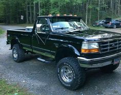 a black pick up truck parked on top of a gravel road in front of trees