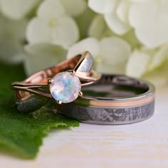 two wedding rings sitting next to each other on top of green leaves and white flowers