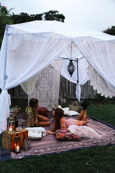 two women sitting on a blanket under a white tent with lights in the back ground