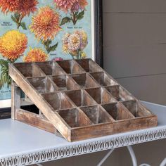 a wooden tray with compartments on top of a white table next to a framed painting