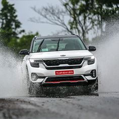 a white car driving through some water on a road with trees in the back ground