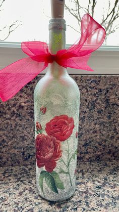 a glass bottle with flowers painted on it and a pink ribbon tied around the top