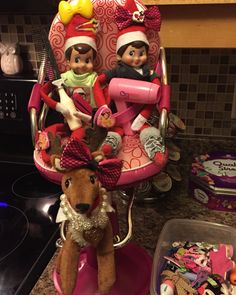 two elf dolls sitting on top of a pink chair next to a pile of toys