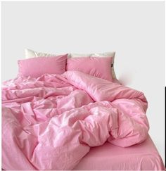 a bed with pink sheets and pillows on top of it in front of a white wall