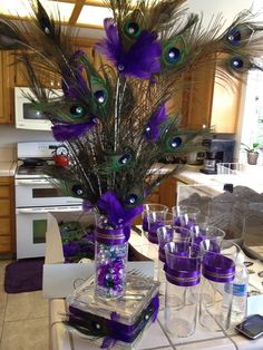 a vase filled with purple and green feathers on top of a table next to glasses