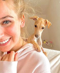 a woman holding a small dog in her arms and smiling at the camera while sitting on a couch